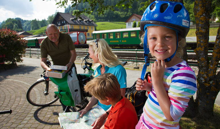 Familie mit Fahrrädern an einer Bahnhofsstation der historischen Muralbahn.