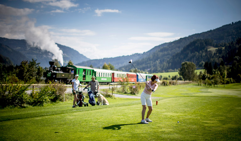 Die historische Muralbahn fährt an der grünen Landschaft eines Golfplatzes vorbei.