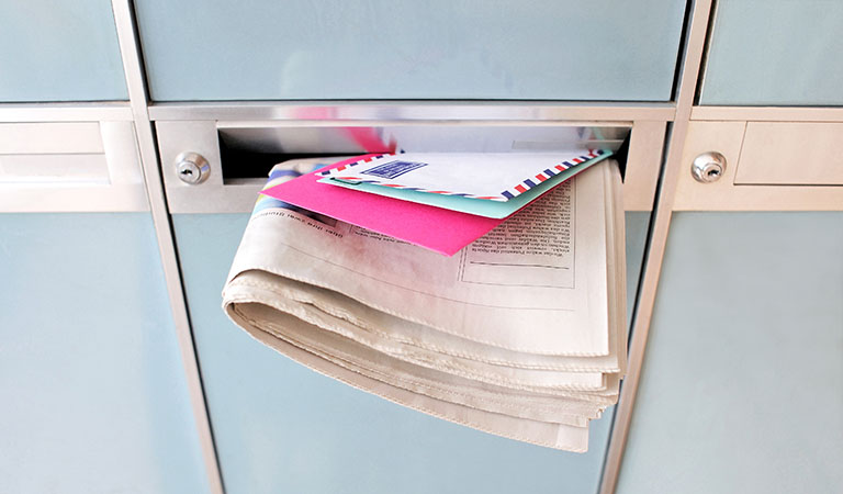 Ein überquellender Briefkasten mit Zeitung und Briefen in einem Mehrfamilienhaus ist ein sicheres Zeichen für Einbrecher, dass die Bewohner gerade im Urlaub sind.
