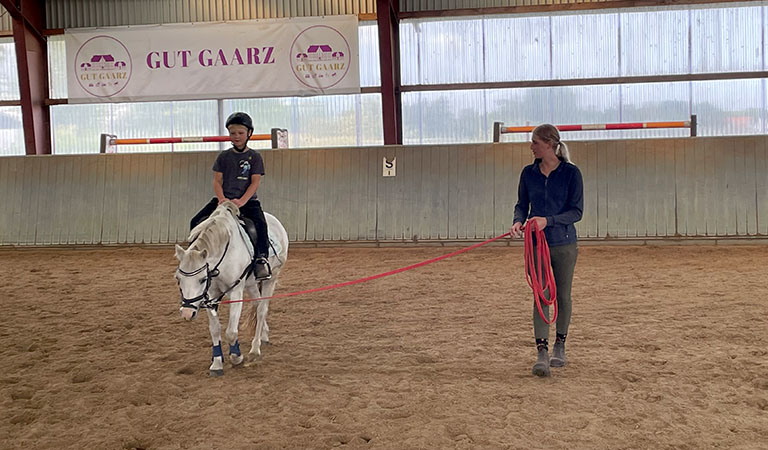 Reitlehrerin mit Reitschüler in einer Reithalle auf einem Reiterhof.