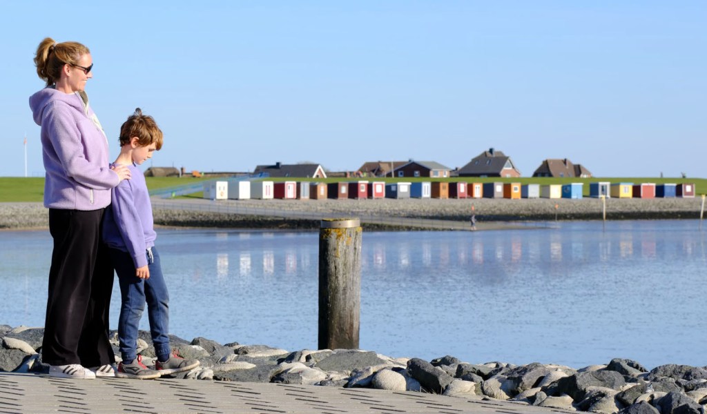Mutter mit Kind am Meer von Dagebüll mit Blick auf die bunten Strandhäuser.