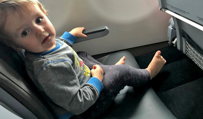 Die Füße eines Kindes liegen auf einer aufblasbaren Sitzverlängerungdie vor dem Flugzeugsitz gestellt ist.