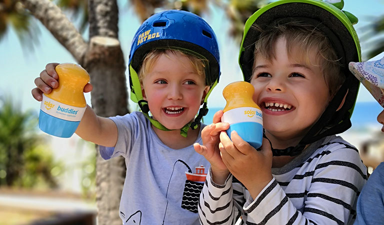 Zwei fröhliche Kinder mit Fahrradhelm und einer der Solar Buddies Flaschen in der Hand zum leichten eincremen mit Sonnencreme.