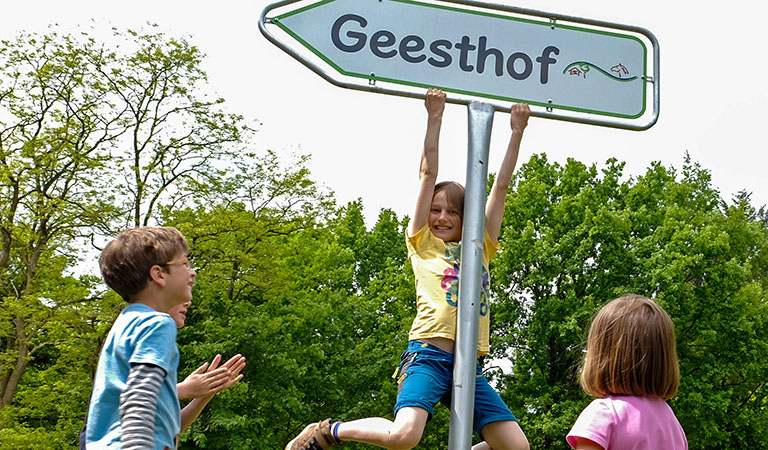 Kinder spielen am Verkehrsschild mit dem Hinweisschild Ferienpark Geesthof in Niedersachsen in Deutschland.