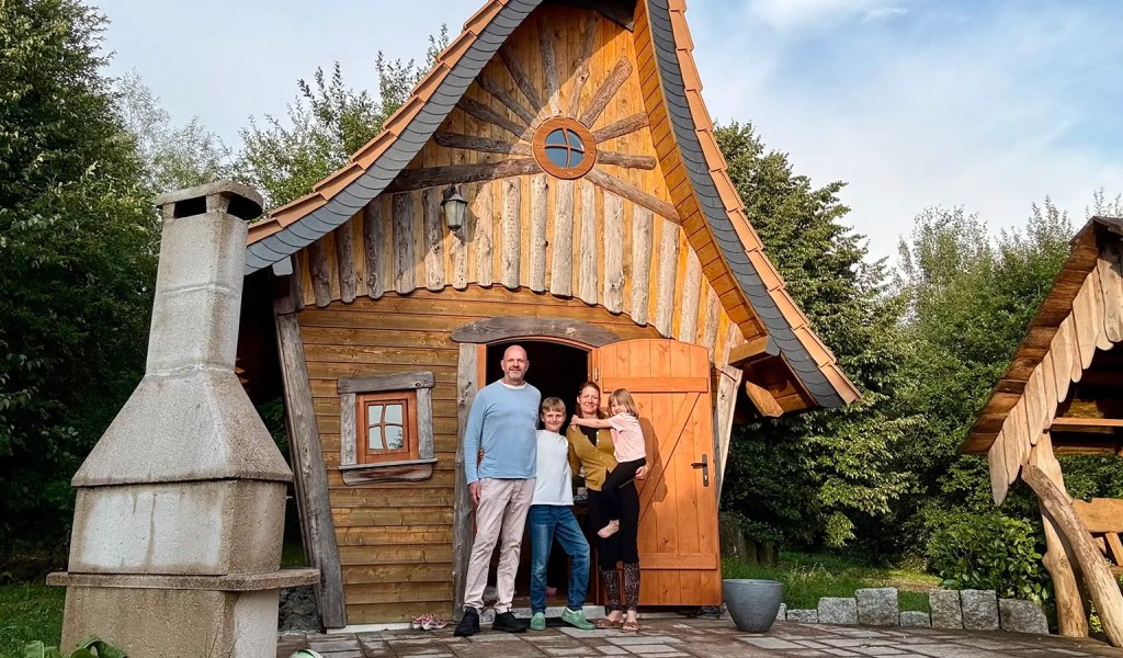 Eine Familie vor ihrer Unterkunft, einem Hexen-Chalet im Feriendorf Auenland in Waffenrod.
