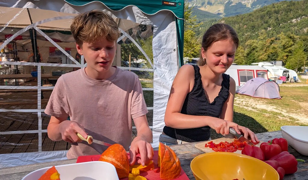 Kinder schneiden Gemüse beim Küchendienst im Familien-Sportcamp in Slowenien.