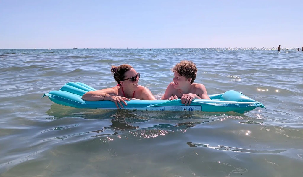 Mutter und Sohn teilen sich eine Luftmatratze im italienischen Meer bei einem Ausflug vom Familien-Sportcamp in Slowenien.