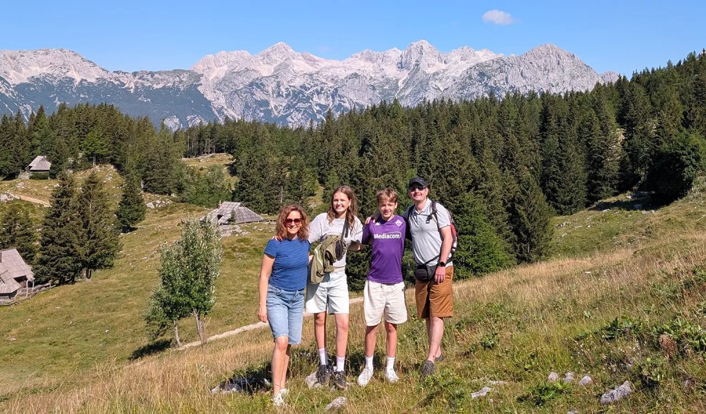 Eine Familie steht vor einem Panorama des Berggebiets Velika Planina am Südrand der Steiner Alpen in Slowenien.