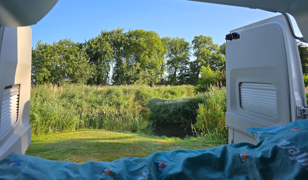 Blick aus den Hecktüren eines Campers auf eine grüne Landschaft.