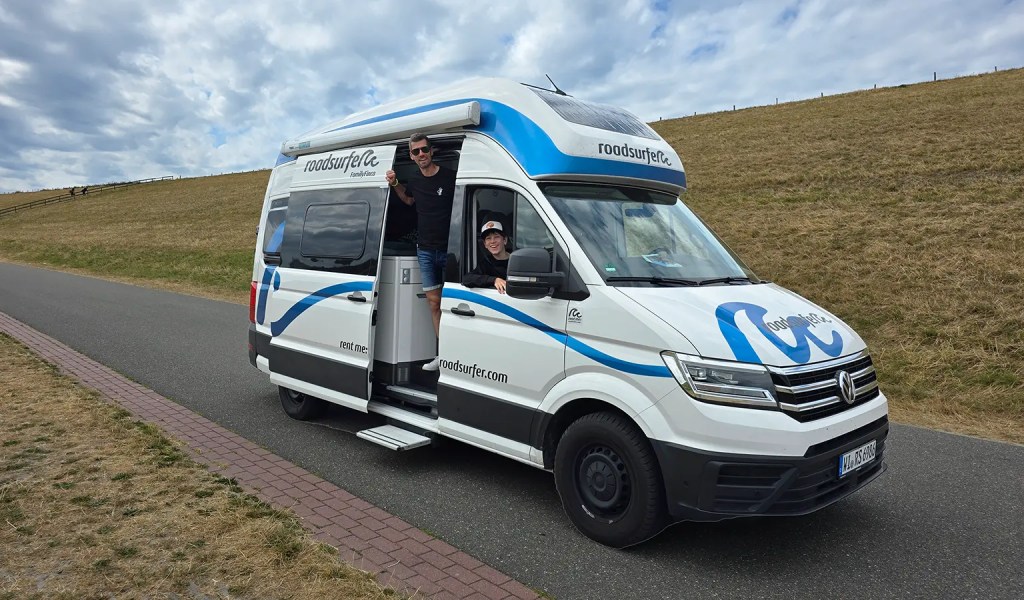 Vater und Sohn schauen aus dem Camper von dem Unternehmen Roadsurfer.